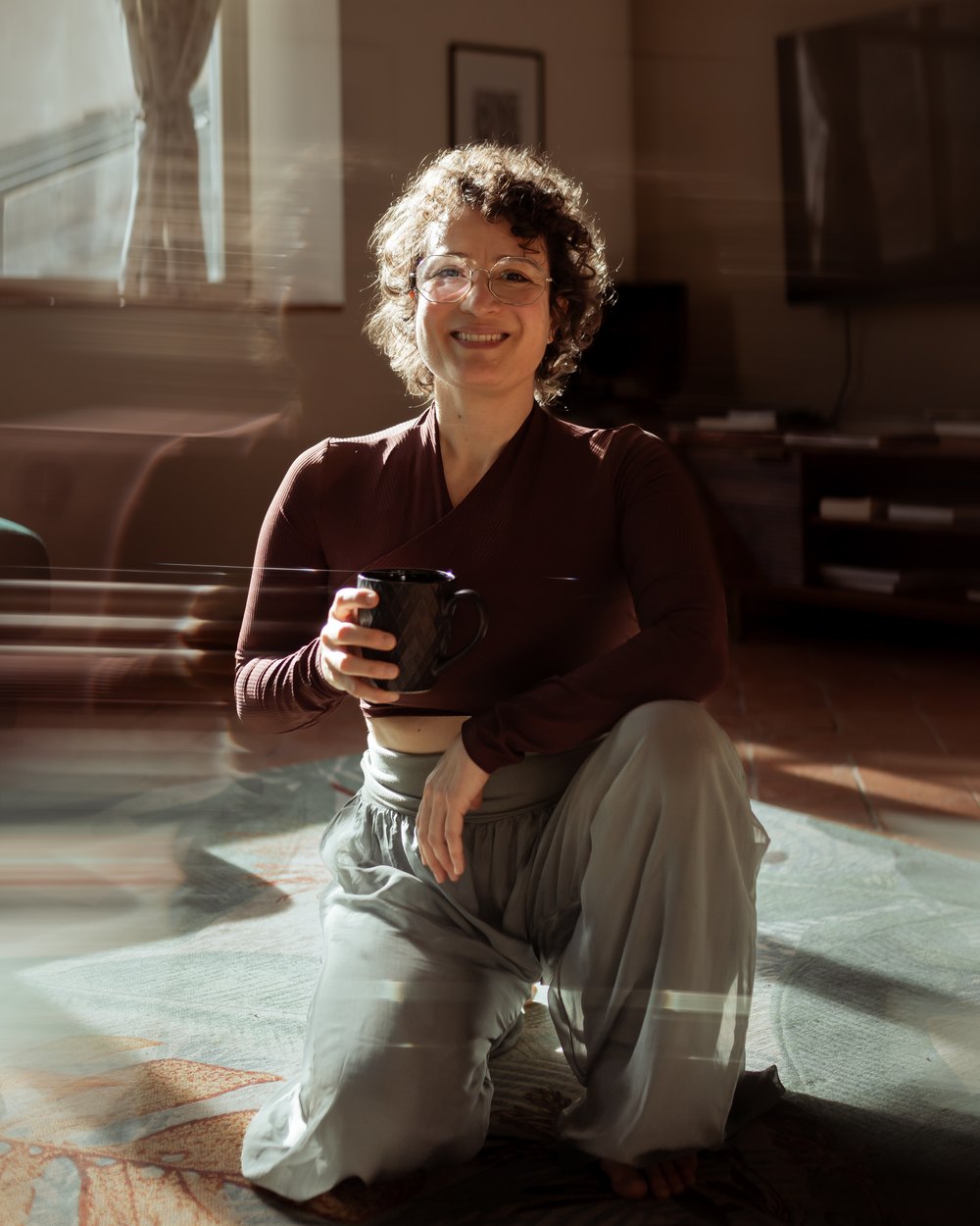 Elena Visentin, fondatrice di KoelPilates, in ginocchio sul tappeto con la sua tazza fra le mani, sorride guardando in camera